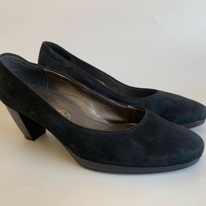 May include: A pair of black suede heeled pumps with a block heel.