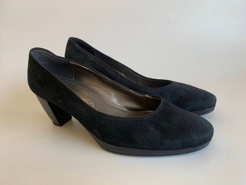 May include: A pair of black suede heeled pumps with a block heel.