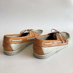 May include: A pair of light grey and brown leather boat shoes with laces. The shoes have a white rubber sole.