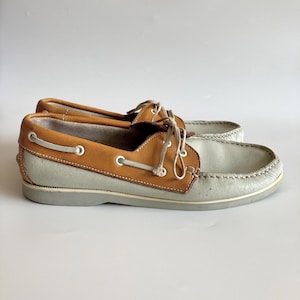 May include: A pair of light gray leather boat shoes with brown leather trim and laces.