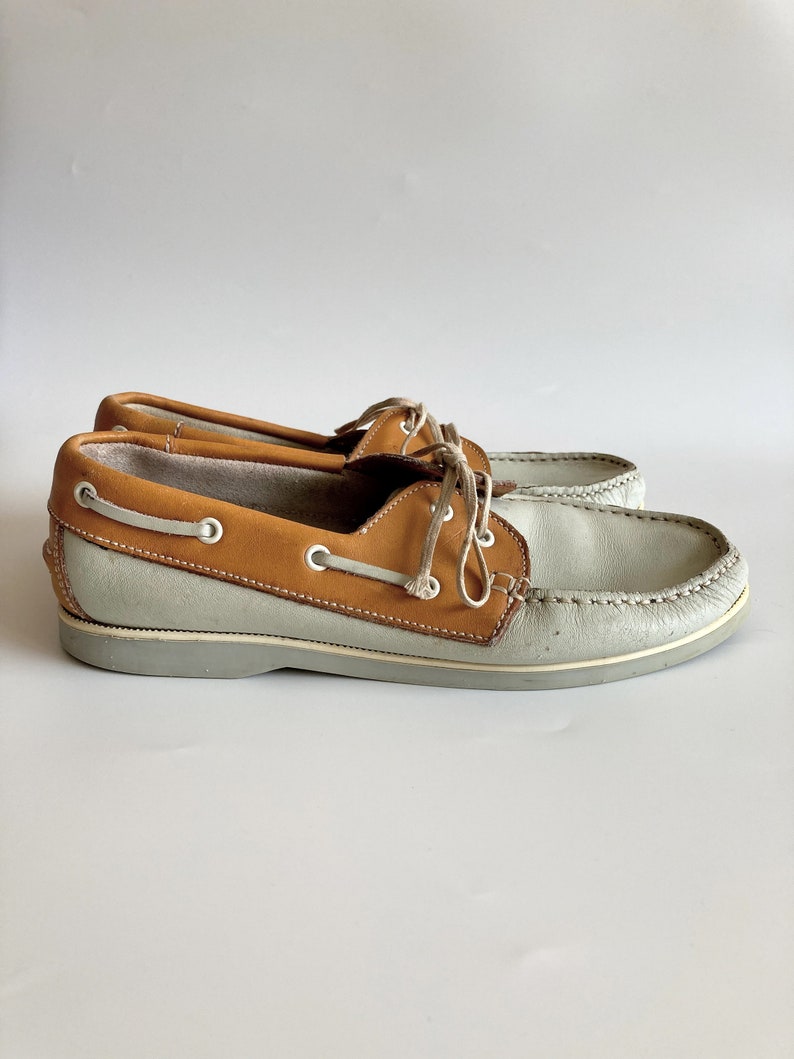 May include: A pair of light gray leather boat shoes with brown leather trim and laces.