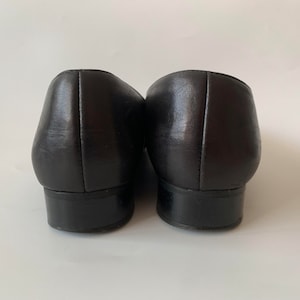 K&ouml;nnte beinhalten: Ein Paar schwarze Leder-Slipper mit abgerundeter Spitze und niedrigem Absatz.