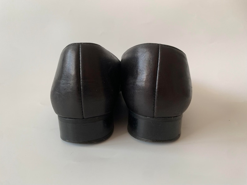 K&ouml;nnte beinhalten: Ein Paar schwarze Leder-Slipper mit abgerundeter Spitze und niedrigem Absatz.