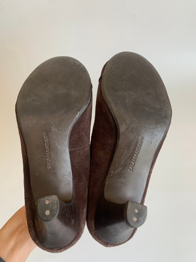 May include: A pair of brown suede heeled shoes with a black rubber sole. The shoes are labeled "Salamander" on the sole.