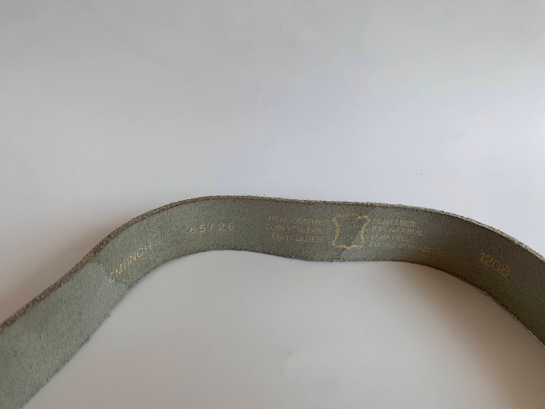 Pu&ograve; includere: Una cintura in pelle grigia chiaro con il testo "65/26 CM/INCH" e "1208" stampato su di essa. La cintura ha anche il testo "GENUINE LEATHER, CONVERTIBLE, REAL LEATHER, ECHT LEDER" stampato su di essa.