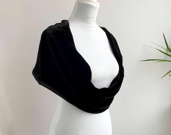 May include: A black velvet shawl draped over a white mannequin. The shawl is a deep, rich black, with a soft, velvety texture. The design is a simple, elegant wrap, perfect for formal occasions or adding a touch of sophistication to any outfit. The mannequin is set against a neutral background.