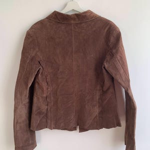 May include: A brown suede jacket with a collared neckline and long sleeves.