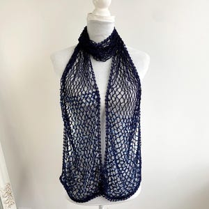 May include: A navy blue, open-weave scarf displayed on a white mannequin. The scarf has a net-like design, creating a delicate and airy appearance. The scarf is draped to showcase its length and texture, suitable for fashion accessories.