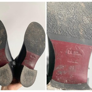 May include: A pair of black boots with textured soles and a dark red heel section. The sole features the embossed text Boss Orange and Made in Italy, with the size 39 clearly visible. The bottom of the boots shows signs of wear and dirt.