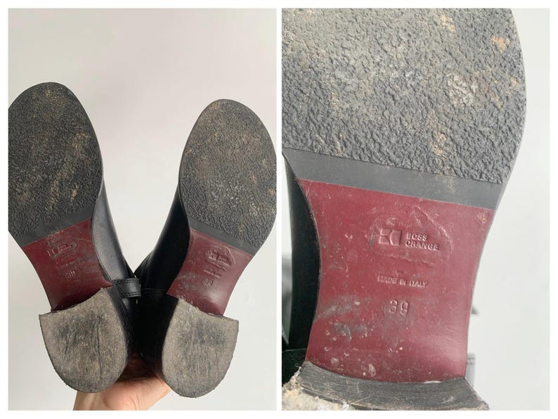 May include: A pair of black boots with textured soles and a dark red heel section. The sole features the embossed text Boss Orange and Made in Italy, with the size 39 clearly visible. The bottom of the boots shows signs of wear and dirt.