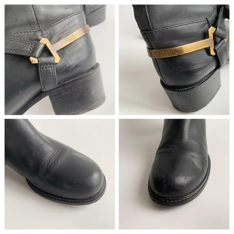 May include: Black leather boots featuring a rounded toe and a low block heel. The ankle area is accented with a decorative gold-tone metal harness strap that includes the embossed text ORANGE HUGO BOSS on the side of the metallic hardware.