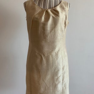 May include: A sleeveless, knee-length dress in a light gold color. The dress has a scoop neckline and a fitted silhouette.