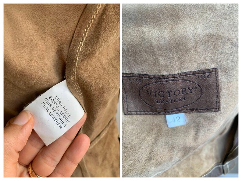 Op de afbeelding: Close-up van de binnenkant van een bruine leren jas. De jas heeft een bruin leren label met de tekst "VICTORY LEATHER" en een maat 12 label. Een wit label met "REAL LEATHER" is ook zichtbaar.