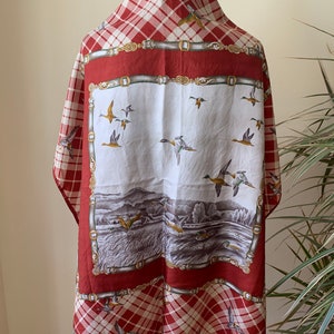 May include: Red and white plaid scarf with a white center panel featuring a scene of ducks flying over a lake and a field. The center panel is bordered by a brown and gold chain design.