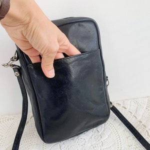 Pu&ograve; includere: Borsa a tracolla in pelle nera con una tasca con cerniera sul davanti. La borsa ha una lunga tracolla regolabile.