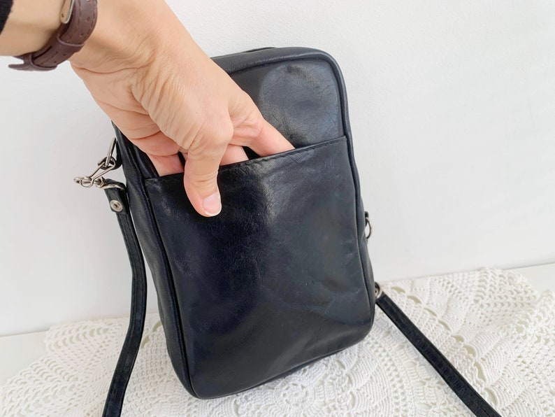 Pu&ograve; includere: Borsa a tracolla in pelle nera con una tasca con cerniera sul davanti. La borsa ha una lunga tracolla regolabile.