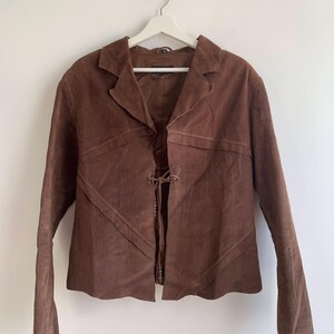 May include: A brown suede jacket with a tie closure at the front. The jacket has a collar and long sleeves.