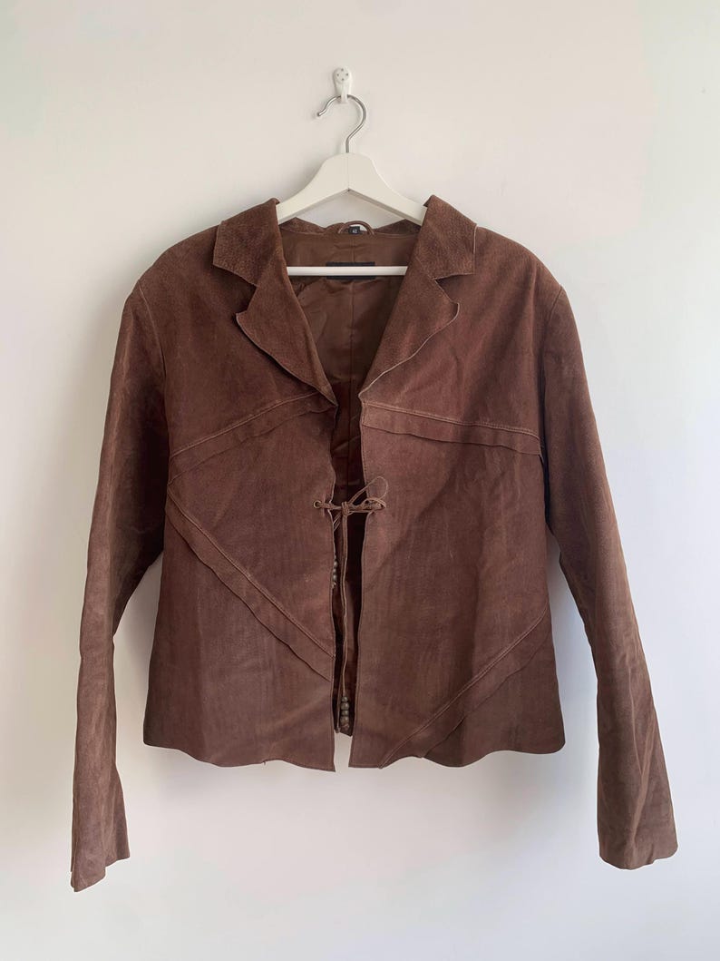 May include: A brown suede jacket with a tie closure at the front. The jacket has a collar and long sleeves.
