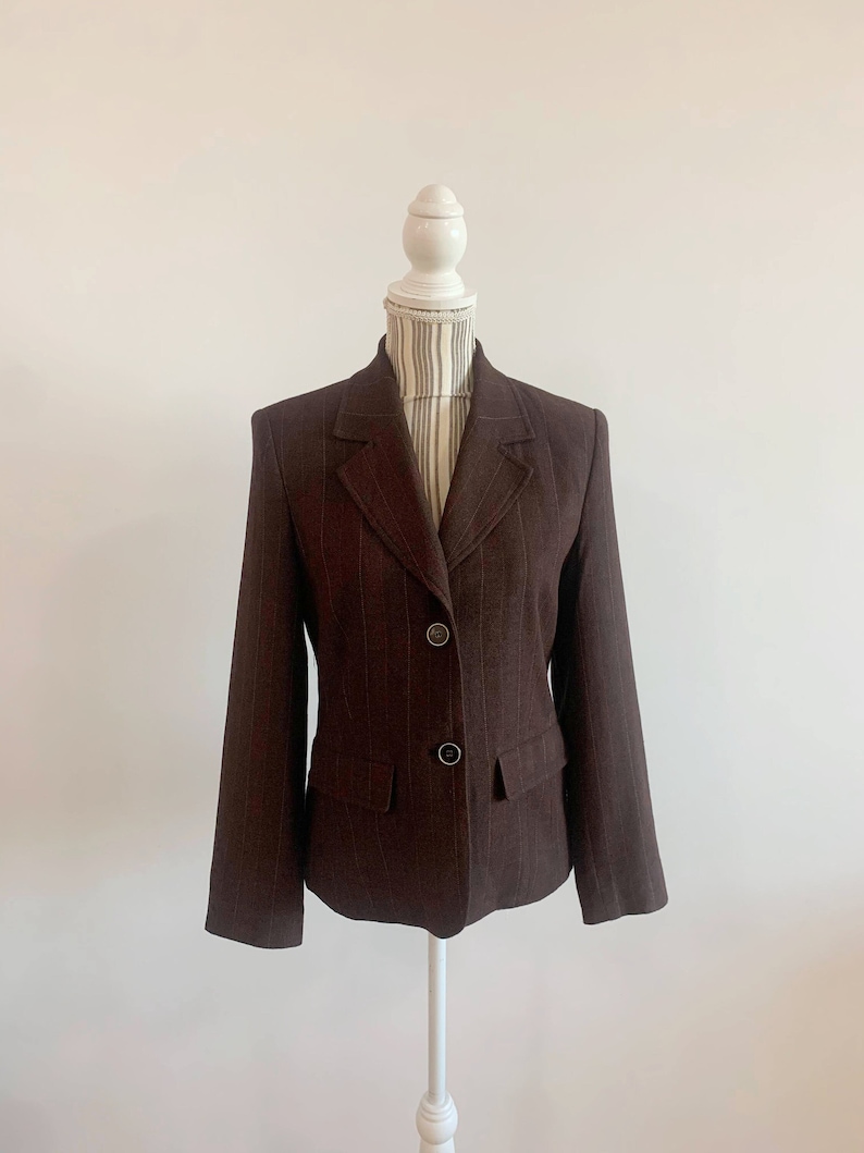 May include: A brown blazer with thin vertical stripes. The blazer has a notched collar, three buttons, and two front pockets.