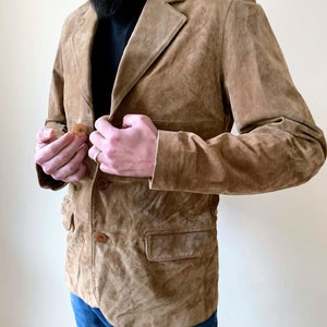 May include: A brown suede jacket with a button closure and two pockets. The jacket has a classic design and is made of a soft, comfortable material.