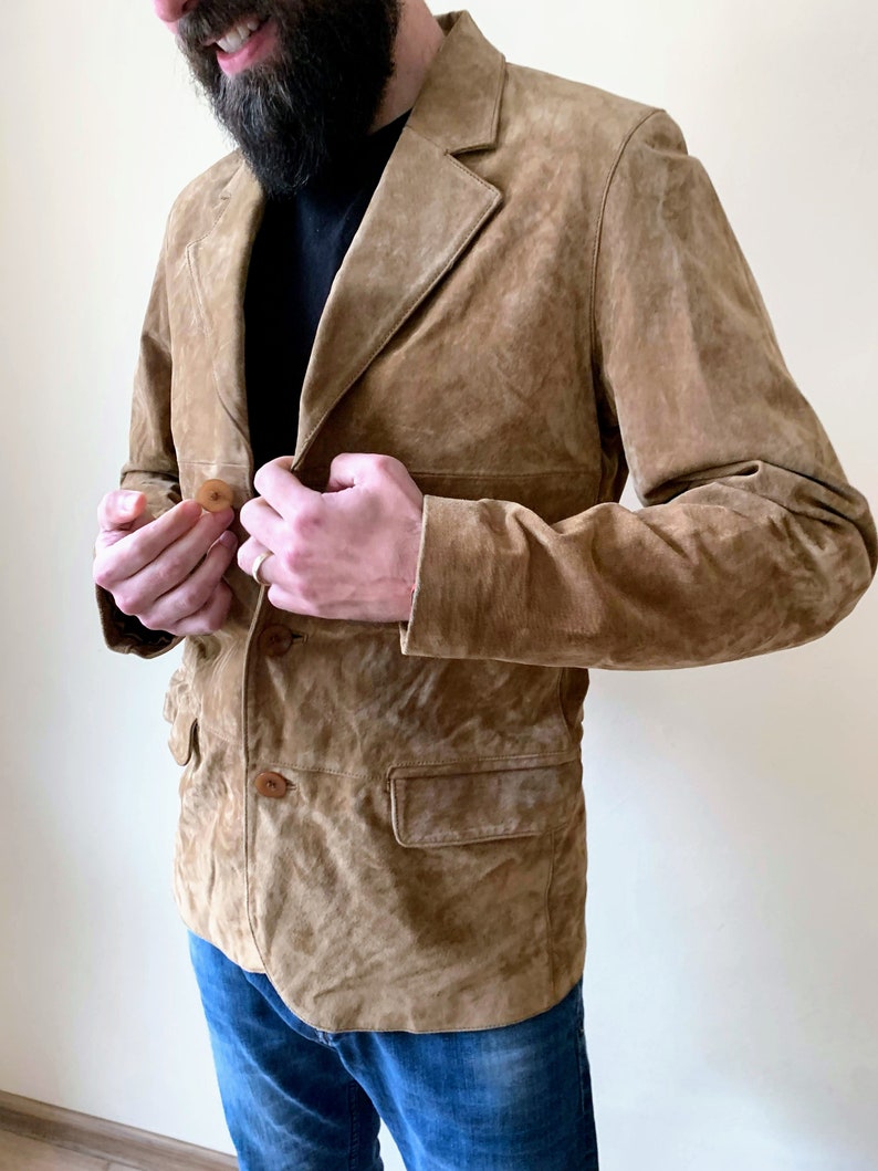 May include: A brown suede jacket with a button closure and two pockets. The jacket has a classic design and is made of a soft, comfortable material.