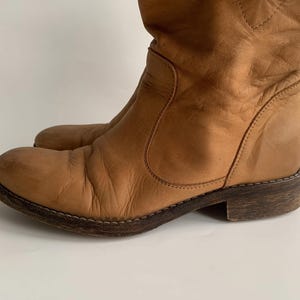 May include: A pair of brown leather knee-high boots with a pointed toe and a low heel.