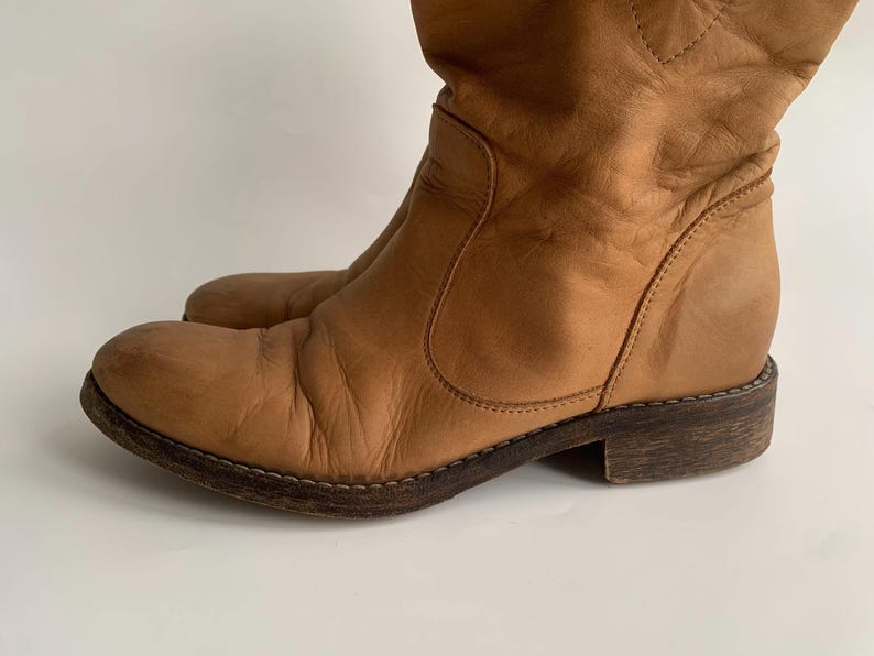 May include: A pair of brown leather knee-high boots with a pointed toe and a low heel.