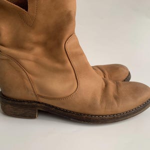 May include: Tan leather ankle boots with a pointed toe and a low heel. The boots have a slouchy, relaxed fit and are made of a soft, supple leather.