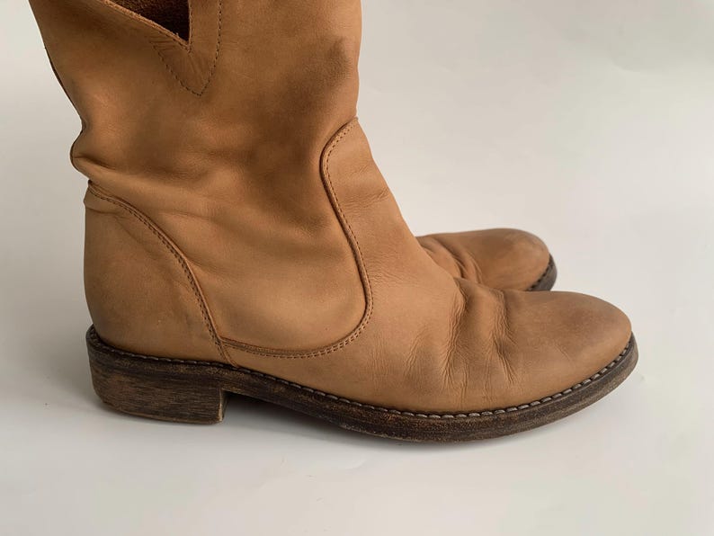 May include: Tan leather ankle boots with a pointed toe and a low heel. The boots have a slouchy, relaxed fit and are made of a soft, supple leather.