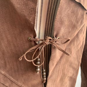 May include: A brown suede jacket with a striped fabric lining and a tie closure with wooden beads.