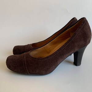 May include: A pair of brown suede heeled pumps with a closed toe and a pointed shape.
