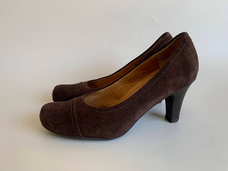 May include: A pair of brown suede heeled pumps with a closed toe and a pointed shape.
