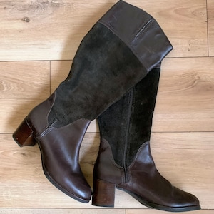 May include: A pair of brown leather knee-high boots with a suede panel on the front and back. The boots have a block heel and a zipper on the inside.
