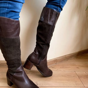 May include: Brown leather and suede knee-high boots with a block heel. The boots have a zipper on the inside of the leg and a brown leather top.