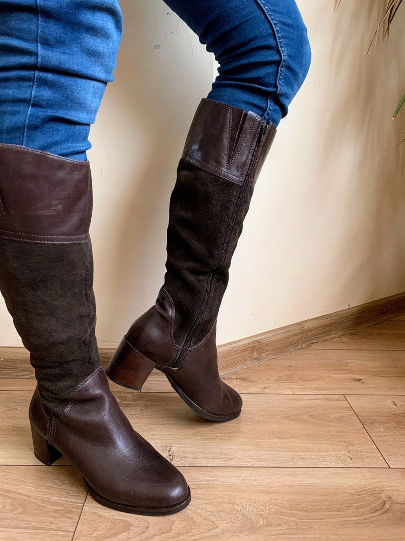 May include: Brown leather and suede knee-high boots with a block heel. The boots have a zipper on the inside of the leg and a brown leather top.