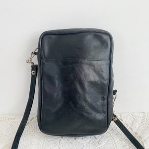 Pu&ograve; includere: Una borsa a tracolla in pelle nera con chiusura a lembo e fibbia argentata. La borsa ha una lunga tracolla regolabile.