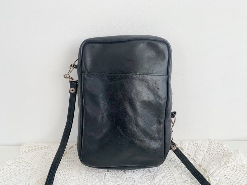 Pu&ograve; includere: Una borsa a tracolla in pelle nera con chiusura a lembo e fibbia argentata. La borsa ha una lunga tracolla regolabile.