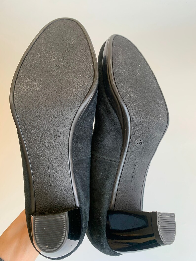 May include: A pair of black suede heeled shoes with a black patent leather heel. The shoes are size 5 1/2.