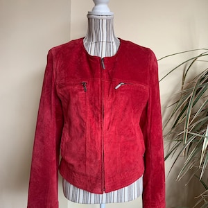 May include: A red suede jacket with a zip fastening and two pockets on the front. The jacket has a round neckline and long sleeves.