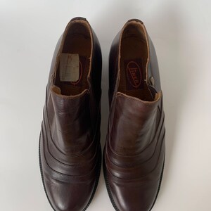 K&ouml;nnte beinhalten: Ein Paar braune Lederstiefeletten mit einem Steppdesign an der Vorderseite. Die Stiefeletten haben eine abgerundete Spitze und einen niedrigen Absatz. Der Markenname "Inner" ist auf der Innenseite des rechten Stiefeletts sichtbar.