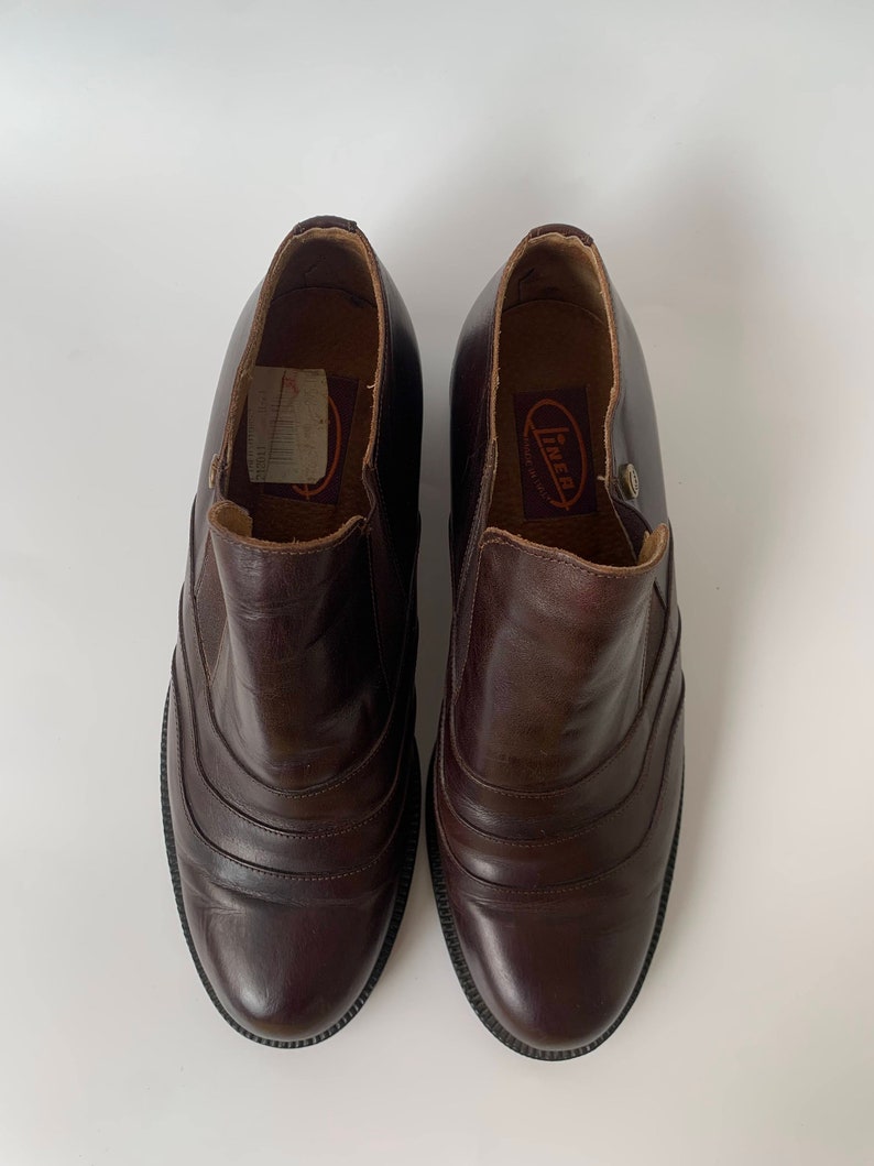 K&ouml;nnte beinhalten: Ein Paar braune Lederstiefeletten mit einem Steppdesign an der Vorderseite. Die Stiefeletten haben eine abgerundete Spitze und einen niedrigen Absatz. Der Markenname "Inner" ist auf der Innenseite des rechten Stiefeletts sichtbar.