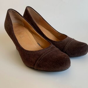 May include: A pair of brown suede heeled shoes. The shoes have a pointed toe and a low heel.