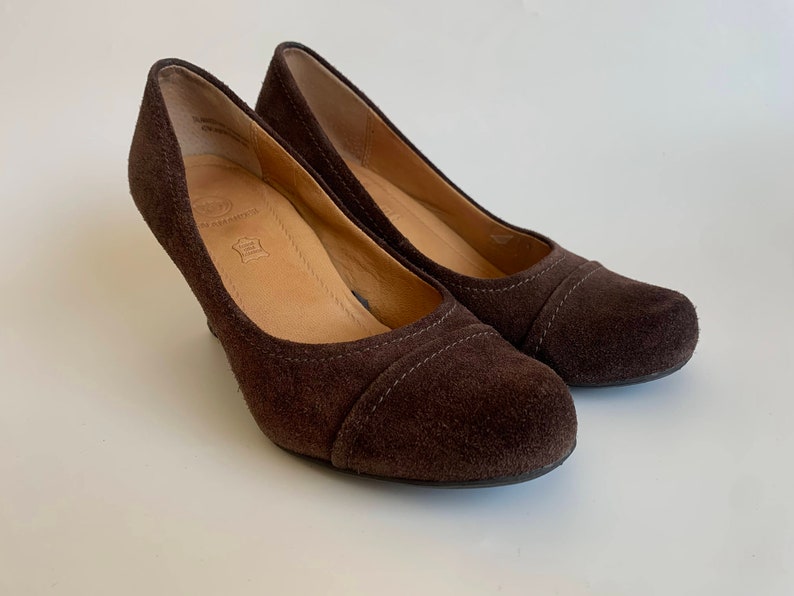 May include: A pair of brown suede heeled shoes. The shoes have a pointed toe and a low heel.