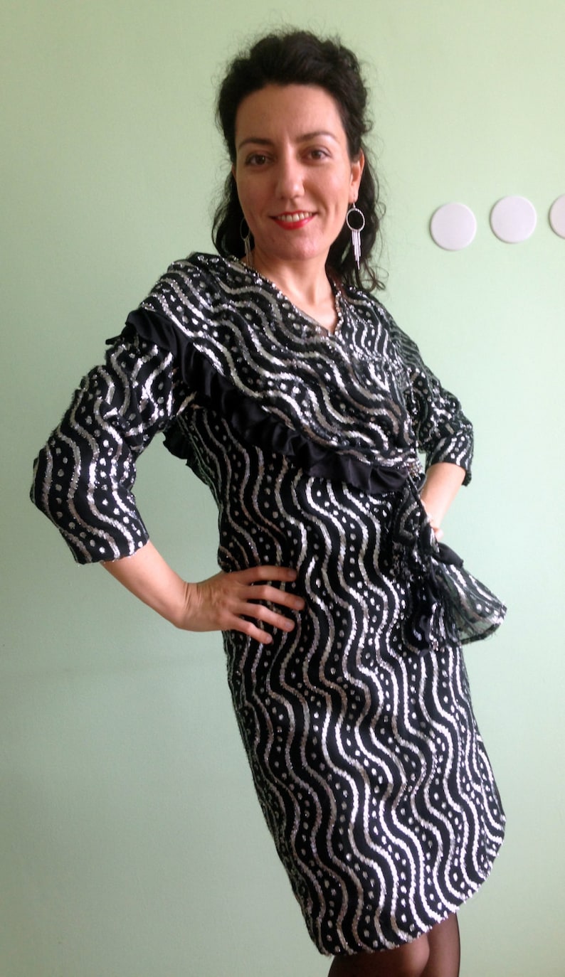 May include: A black and silver sequined dress with a wavy pattern. The dress has a ruffled neckline and a wrap-style closure.