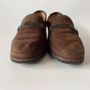 May include: A pair of brown suede loafers with a black metal buckle detail.
