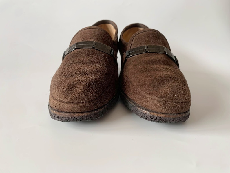 May include: A pair of brown suede loafers with a black metal buckle detail.