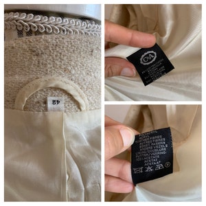 Peut inclure: Un blazer beige avec une &eacute;tiquette noire indiquant "C&A" et la composition du tissu. L'&eacute;tiquette indique &eacute;galement la taille 42. Le blazer est doubl&eacute; de satin blanc.