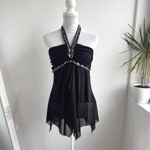 May include: A black halter top featuring a gathered bodice and a sheer, layered handkerchief hem. The neckline and the horizontal band across the chest are embellished with silver-toned sequins and beads, creating a decorative, shimmering accent.