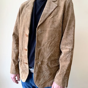 May include: A brown suede jacket with a button-up front and two pockets. The jacket has a classic style and is made of a soft, comfortable material.