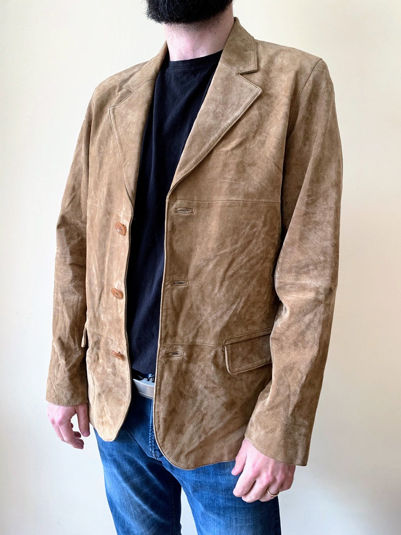 May include: A brown suede jacket with a button-up front and two pockets. The jacket has a classic style and is made of a soft, comfortable material.